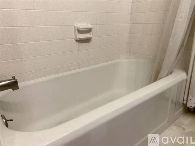 A white bathtub in a bathroom with a white tiled wall.