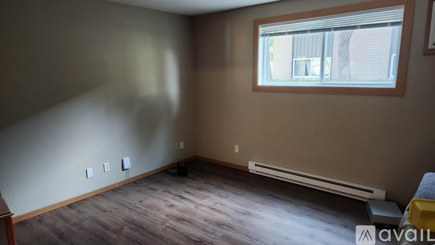 A room with a window, a wall-mounted air conditioner, and a wooden floor.