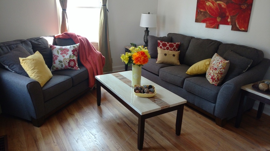 A living room with a grey couch, a coffee table with a vase of flowers, and a red blanket.