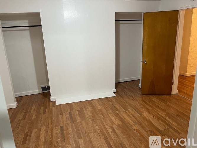 A room with wooden flooring and white walls, with a door on the right.