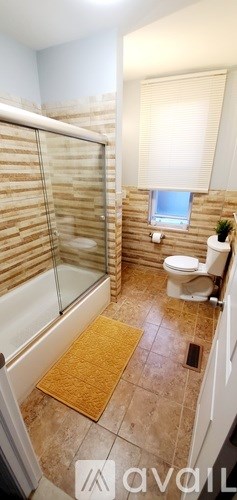 A bathroom with a toilet, a window with blinds, and a glass shower stall.
