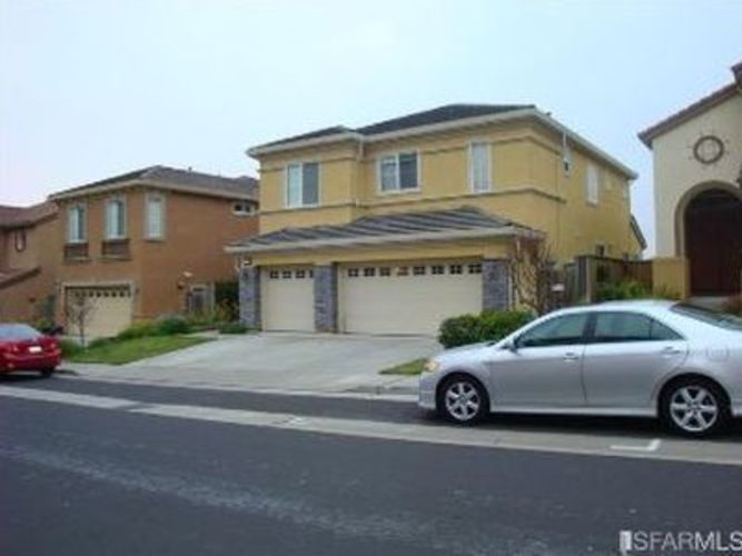 A silver car is parked in front of a yellow house.