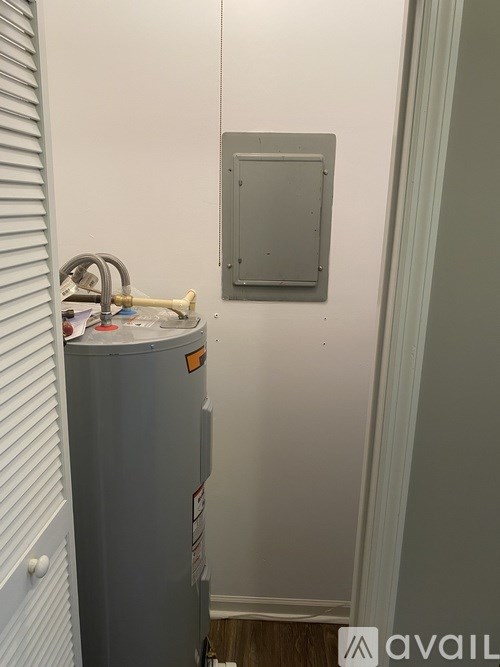 A grey water heater is in a room with a white wall and a grey electrical box.