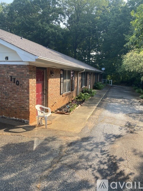 A small house with a red door and a white chair in front of it.