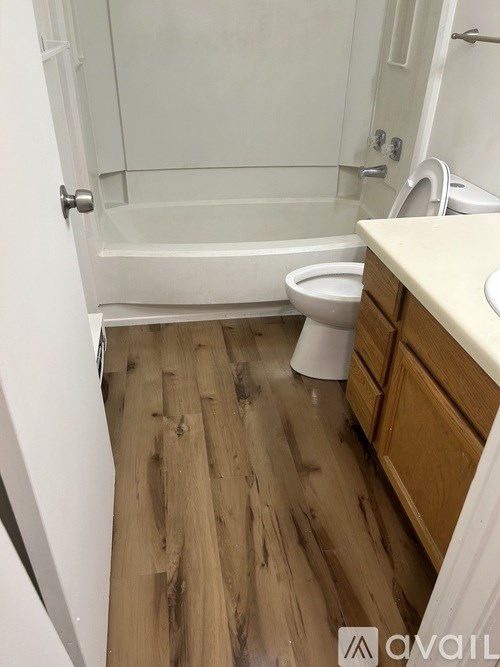 A bathroom with a toilet, sink, and wooden floor.