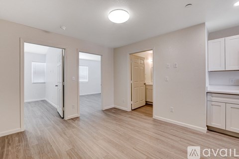 A spacious room with wooden flooring and white walls, featuring a kitchen area with cabinets and a countertop.