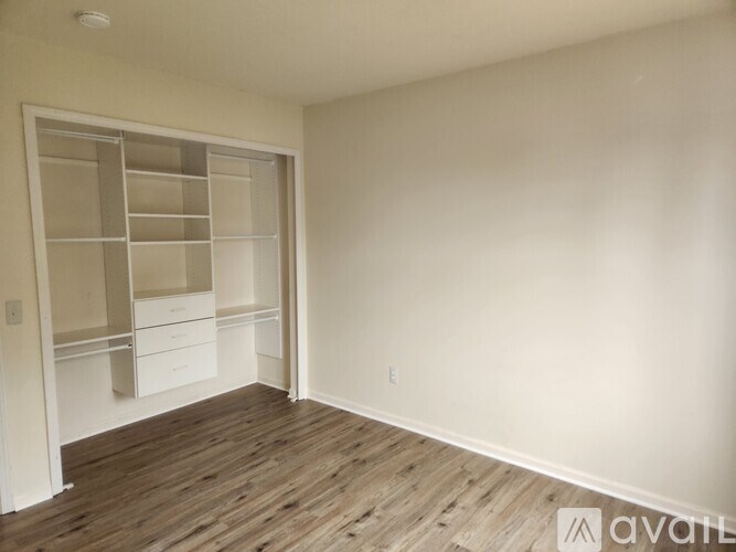 A room with a white wall and a wooden floor with a white cabinet and drawers.