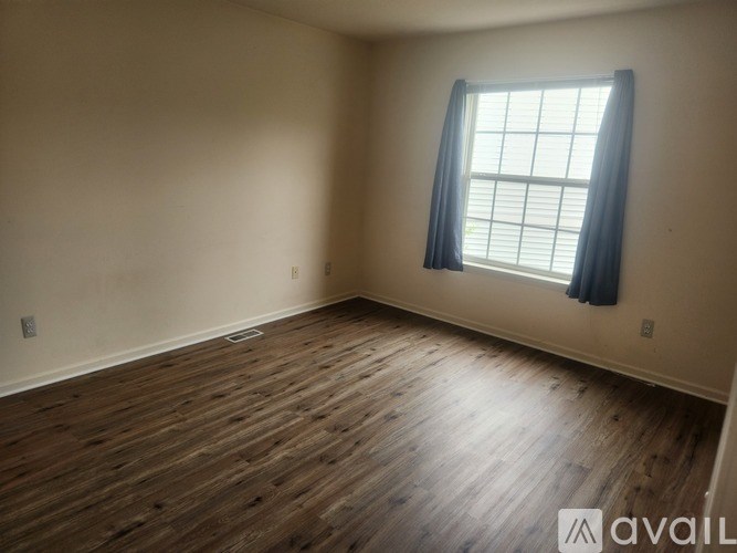 A room with wooden flooring and a window with blue curtains.