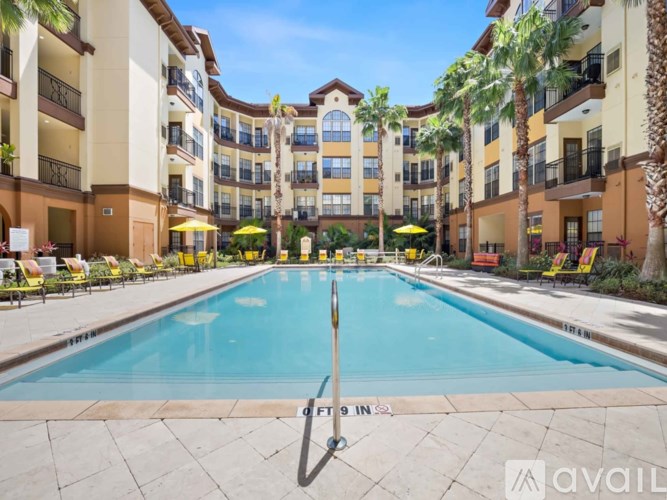 A large pool in the middle of a courtyard surrounded by palm trees and lounge chairs.