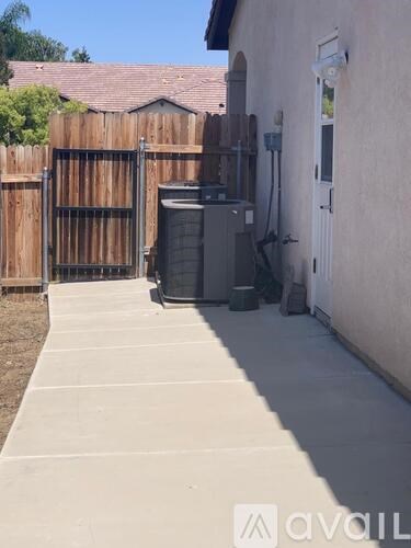 A concrete walkway leads to a gate and a utility box outside a house.