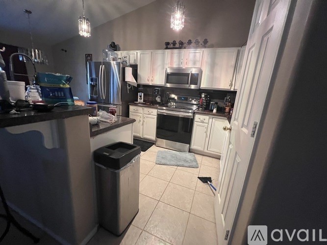 A kitchen with a black fridge, white cabinets, and a black trash can.