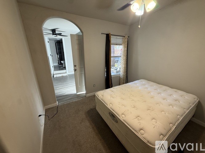 A bedroom with a bed, a window with curtains, and a ceiling fan.