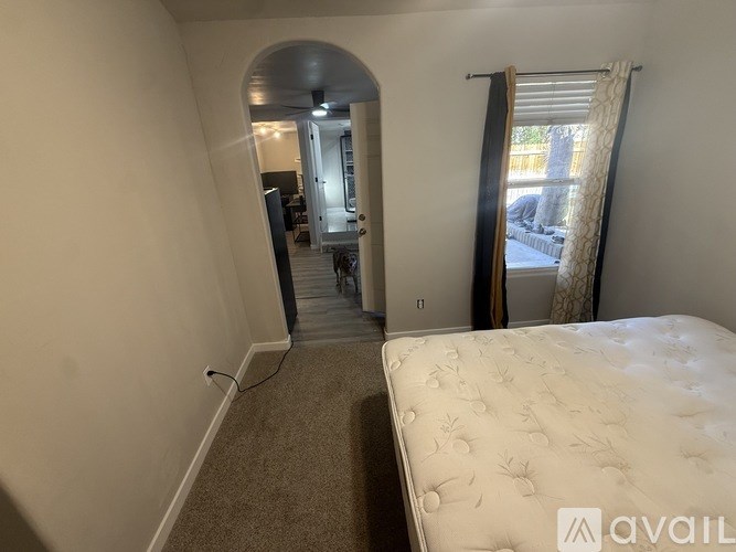 A bedroom with a bed, a window with curtains, and a hallway leading to another room.