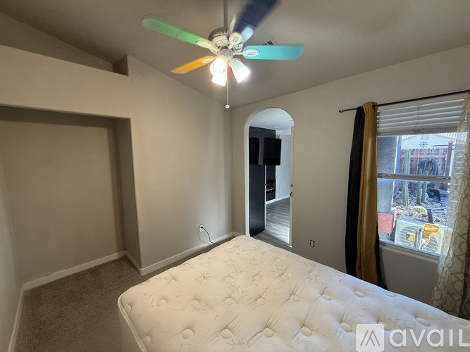 A bedroom with a bed, a ceiling fan, and a window with a view of the outside.