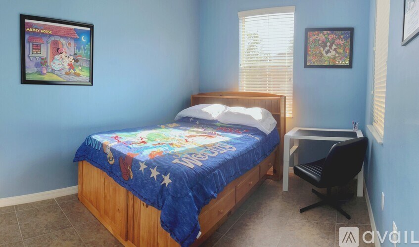 A bedroom with a bed, desk, and two pictures on the wall.