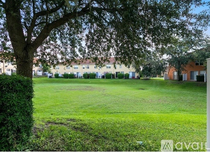 A grassy field with a tree on the left and houses in the background.