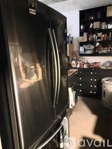 A black refrigerator with a stainless steel handle sits in a kitchen.