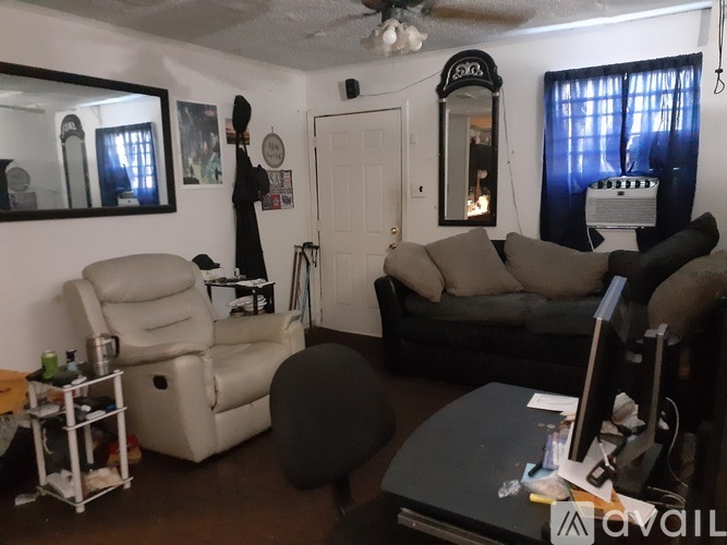 A living room with a white chair, a black ottoman, and a grey couch.