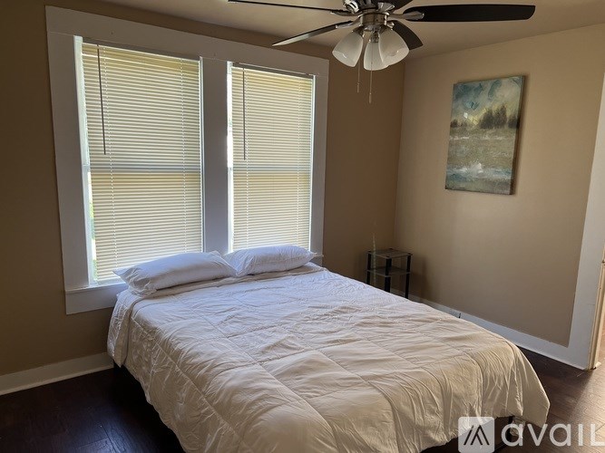 A bedroom with a bed, a ceiling fan, and a painting on the wall.