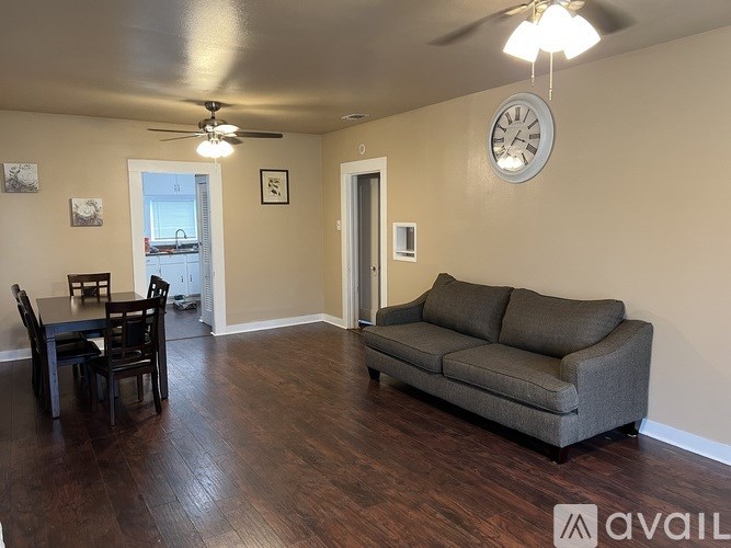 A living room with a grey couch, a dining table with chairs, and a ceiling fan.