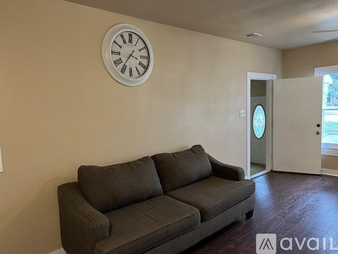 A living room with a brown couch and a clock on the wall.