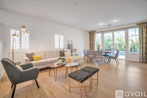 A living room with a grey armchair, a white sofa, a coffee table, and a dining table set up.