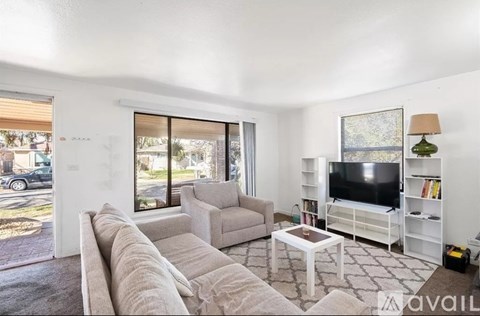 A living room with a grey sofa, a white coffee table, a grey armchair, a television and a bookshelf.