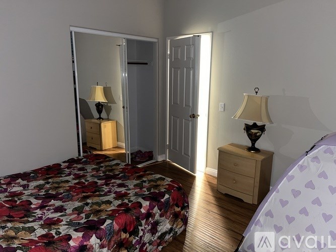A bedroom with a floral bedspread and a wooden dresser with a lamp on top.