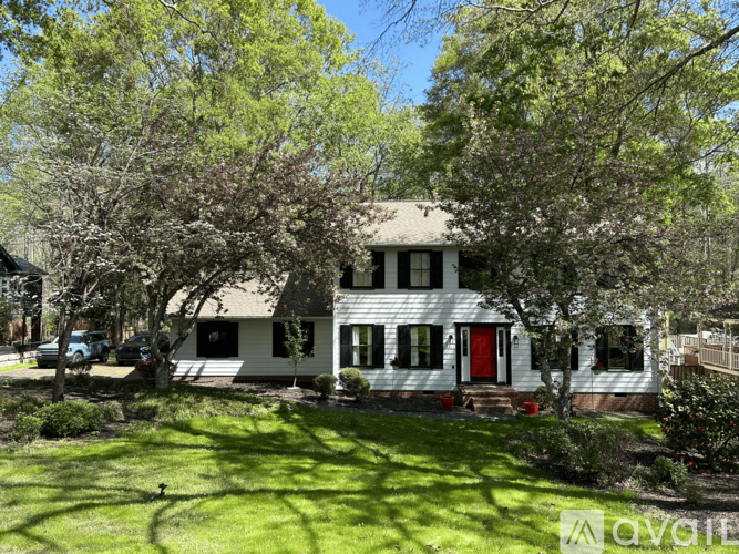 A white house with a red door is surrounded by greenery.