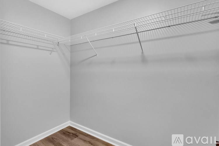 A room with a white wall and a wooden floor with a wire shelving unit.