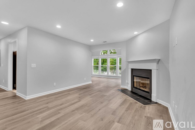 A spacious living room with a fireplace and a view of trees outside the window.