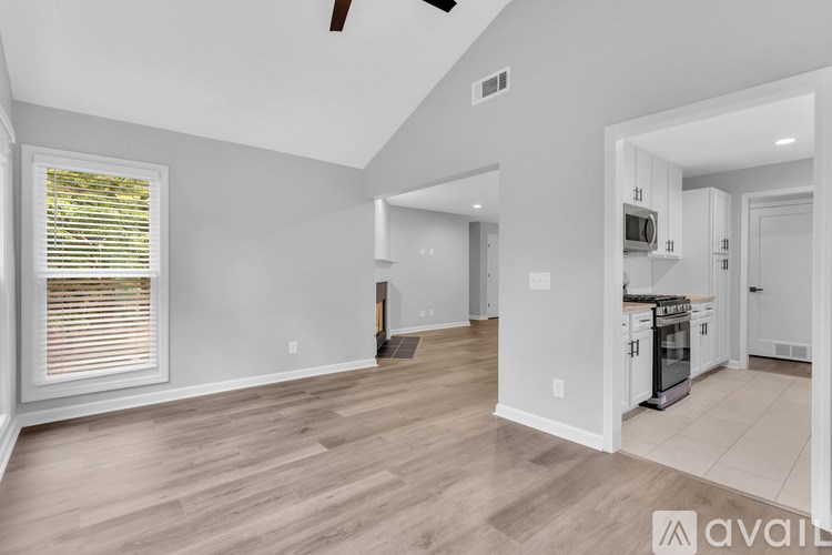 A spacious living room with a ceiling fan and a kitchen area in the background.