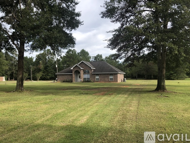 A house is situated in a grassy field with trees in the background.