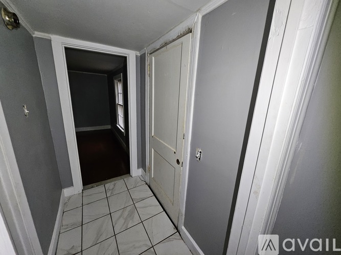 A hallway with a door on the right and a doorway leading to another room on the left.