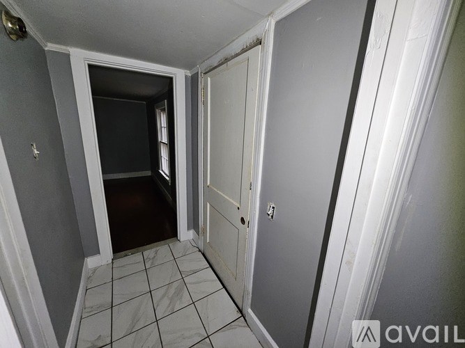 A hallway with a door on the right and a doorway leading to another room on the left.