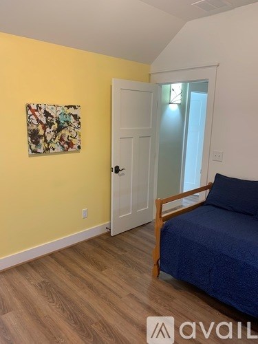 A bedroom with a bed, a painting on the wall, and a door.