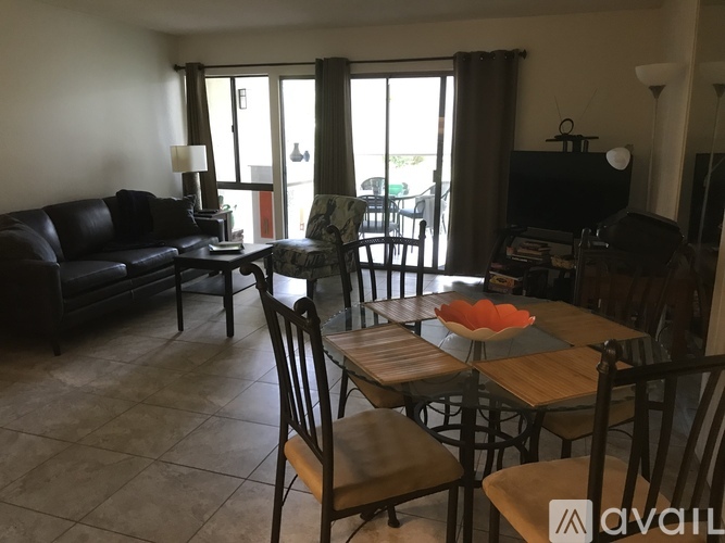 A living room with a black couch, a wooden dining table with chairs, and a television.