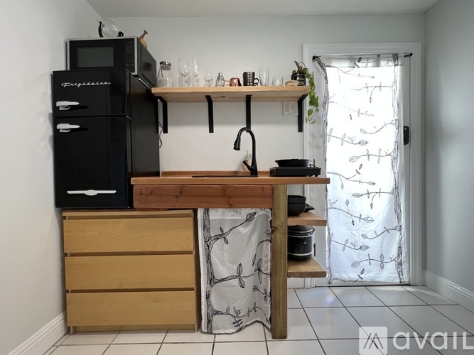 A kitchen with a black fridge, wooden drawers and a counter with a plant on it.