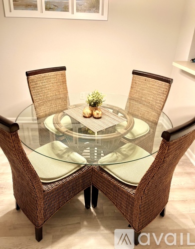 A glass table with wicker chairs and a small plant on top.