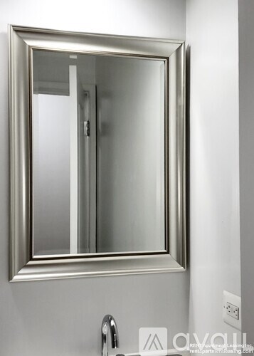 A bathroom mirror with a silver frame is mounted on a white wall.