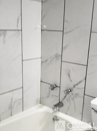 A white bathtub with a silver faucet is in a bathroom with white marble tiles.