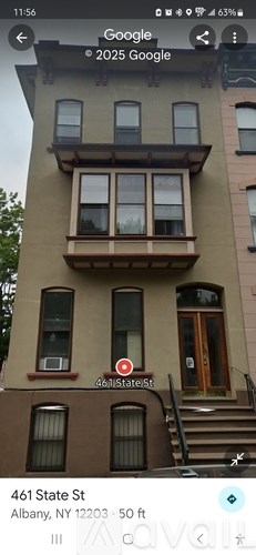 A brown building with a balcony and a window with a curtain.