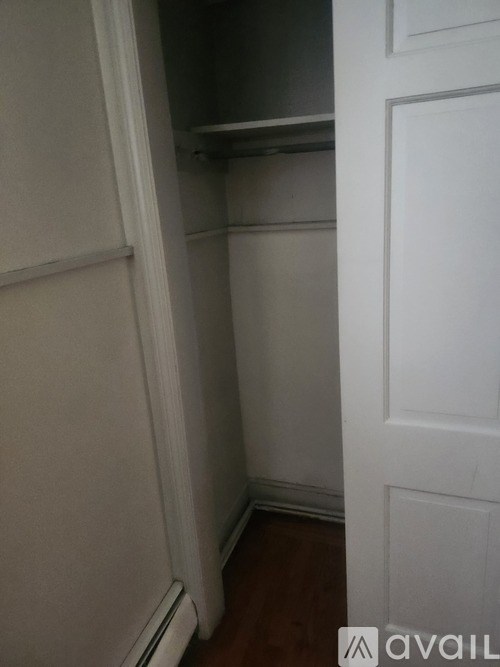 A white door is open to a small, empty room with a wooden floor.