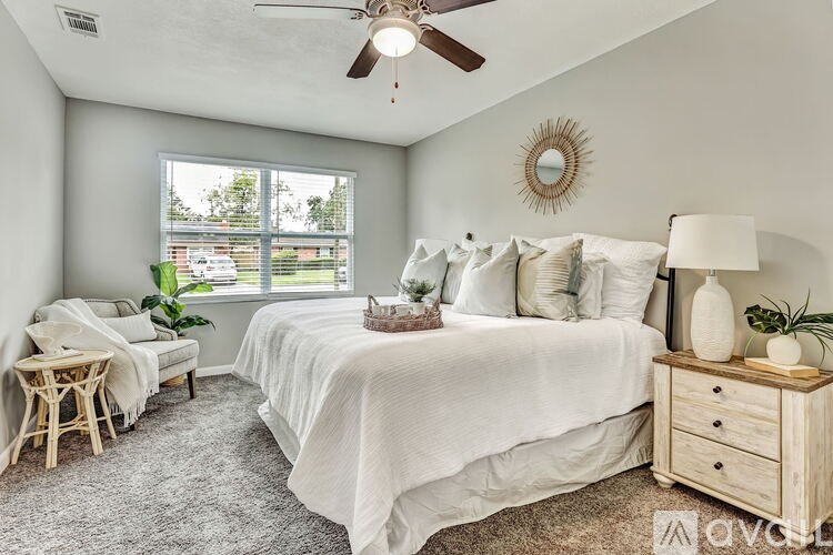 A bedroom with a large bed, a ceiling fan, and a window with a view of a parking lot.