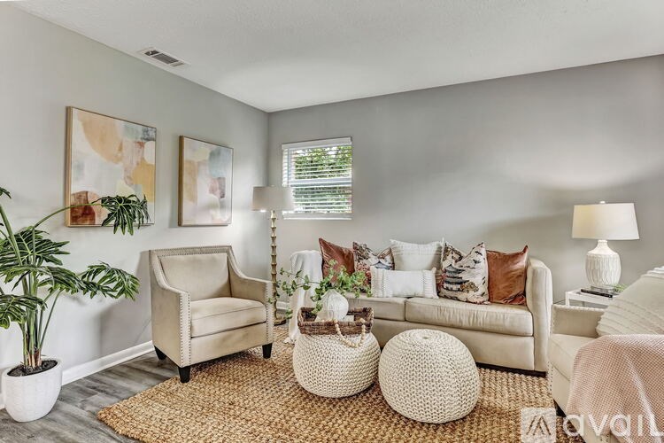 A living room with a beige sofa, a white armchair, and a woven ottoman.