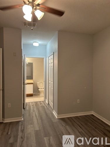 A room with a ceiling fan and a wooden floor leading to a bathroom.