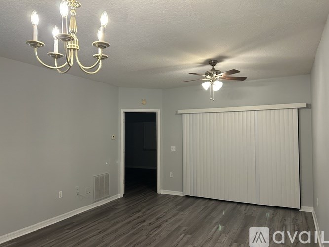 A room with a chandelier, ceiling fan, and a window with blinds.