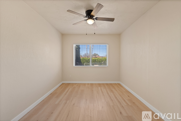 A room with a ceiling fan and a window with a view of a fence and trees.