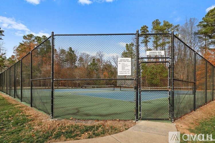 A tennis court is enclosed by a black fence and has a sign on it.