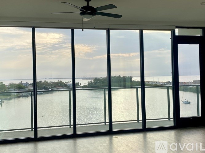 A room with a ceiling fan and large windows overlooking a body of water.